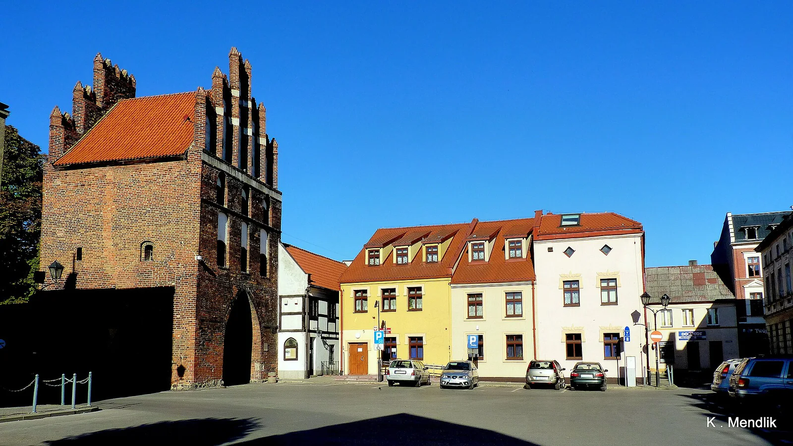 Ceglana Brama Chełmińska w Brodnicy ze schodkowym szczytem i jasnymi kamienicami obok