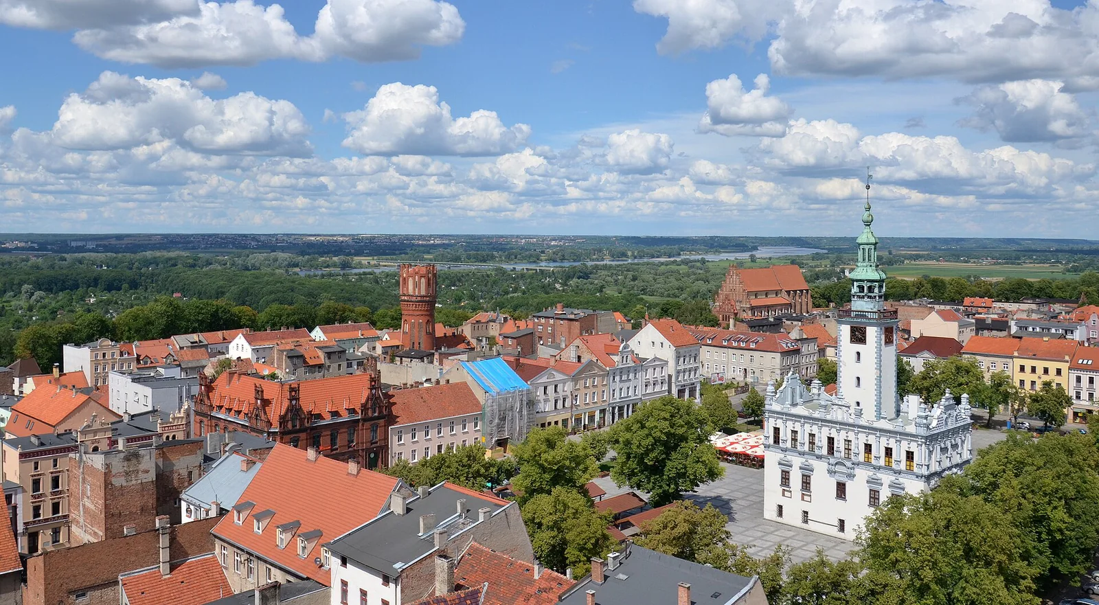Panorama centrum Chełmna z jasnym ratuszem, Rynkiem i czerwonymi dachami pod białymi chmurami