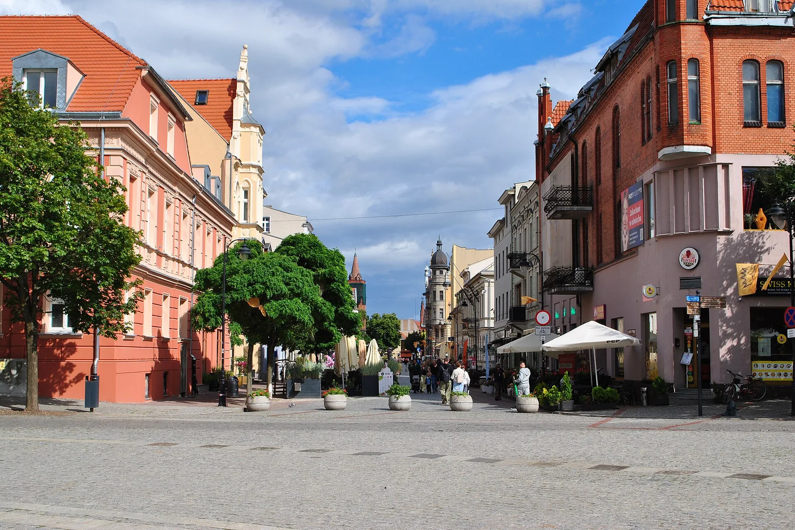 Widok z Rynku na ulicę Bolesława Chrobrego w Gnieźnie, kamienice i drzewa przy deptaku