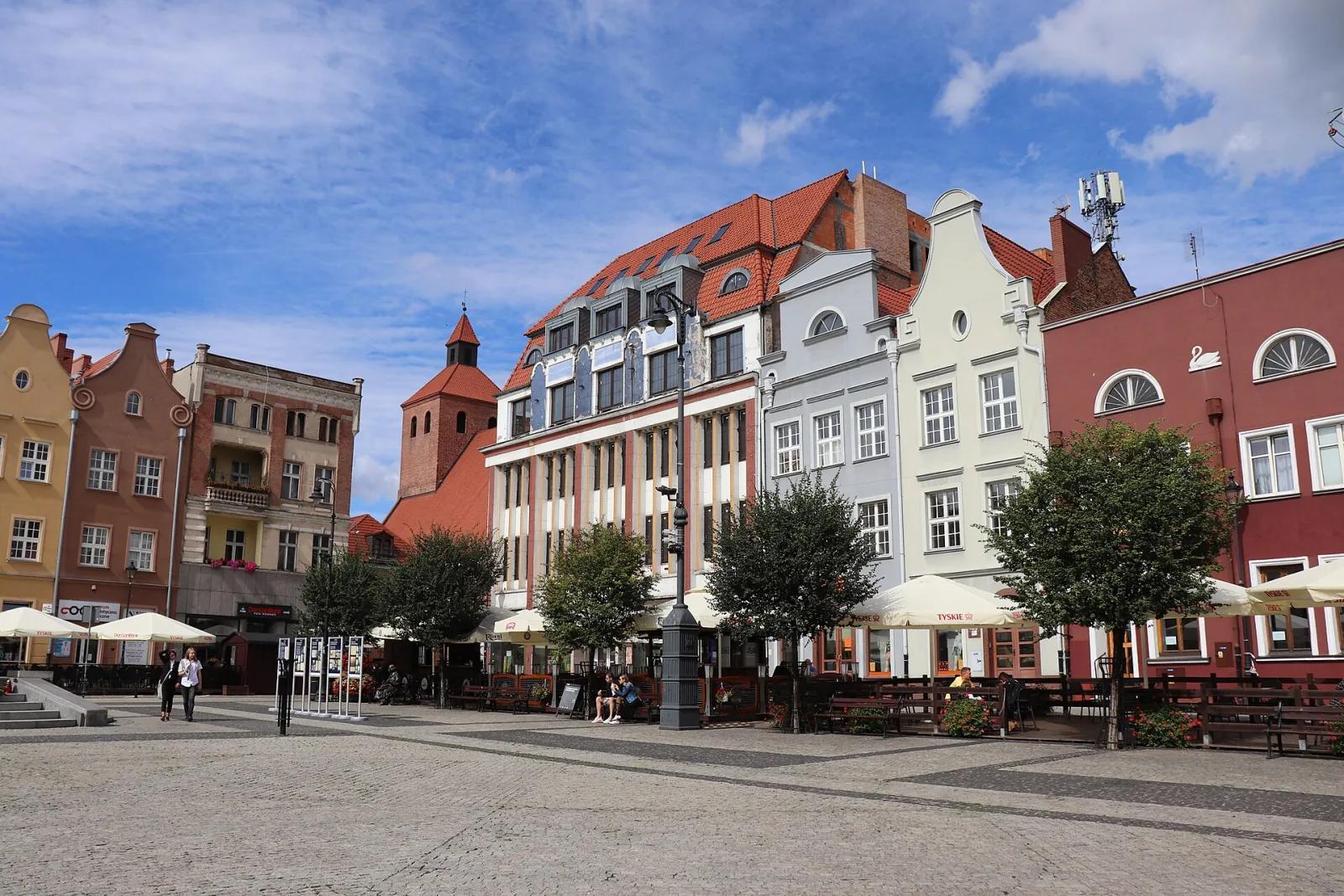 Kolorowe kamienice przy Rynku w Grudziądzu pod błękitnym niebem z białymi chmurami