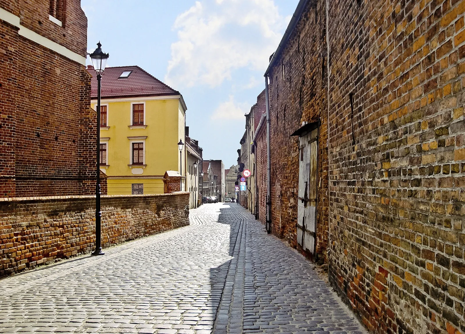 Brukowana ulica Spichrzowa w Grudziądzu pomiędzy ceglanymi ścianami zabytkowej zabudowy