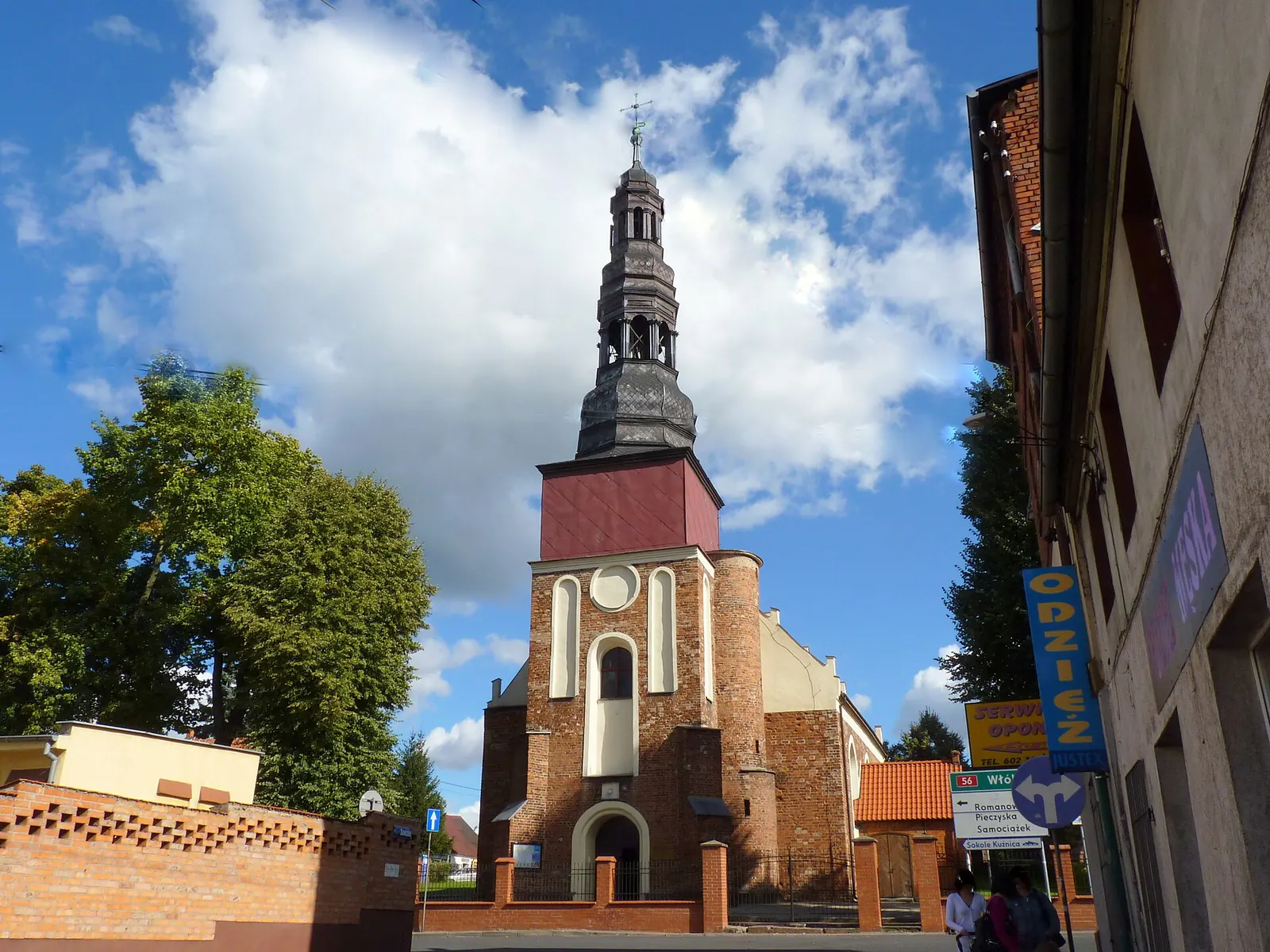 Kościół św. Andrzeja w Koronowie z wysoką wieżą widziany od ulicy pod błękitnym niebem