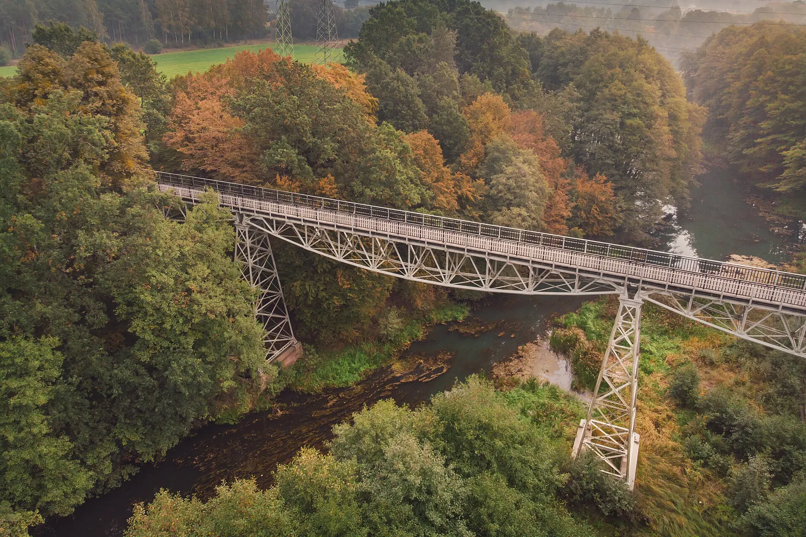 Most dawnej kolei wąskotorowej nad Brdą w Koronowie w otoczeniu drzew o zielonych i jesiennych koronach