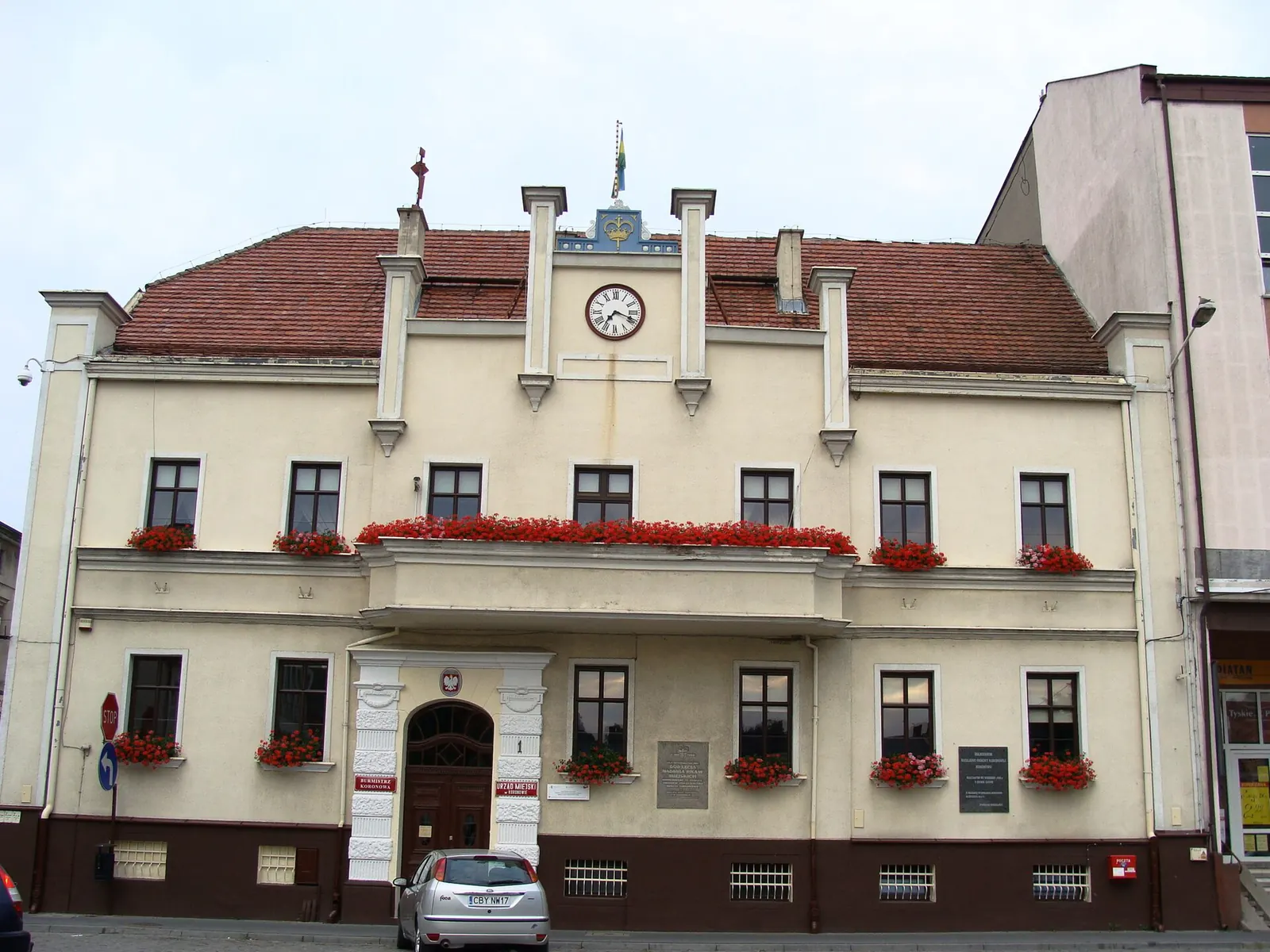 Jasna elewacja ratusza w Koronowie, zegar w środkowym szczycie i czerwony dach