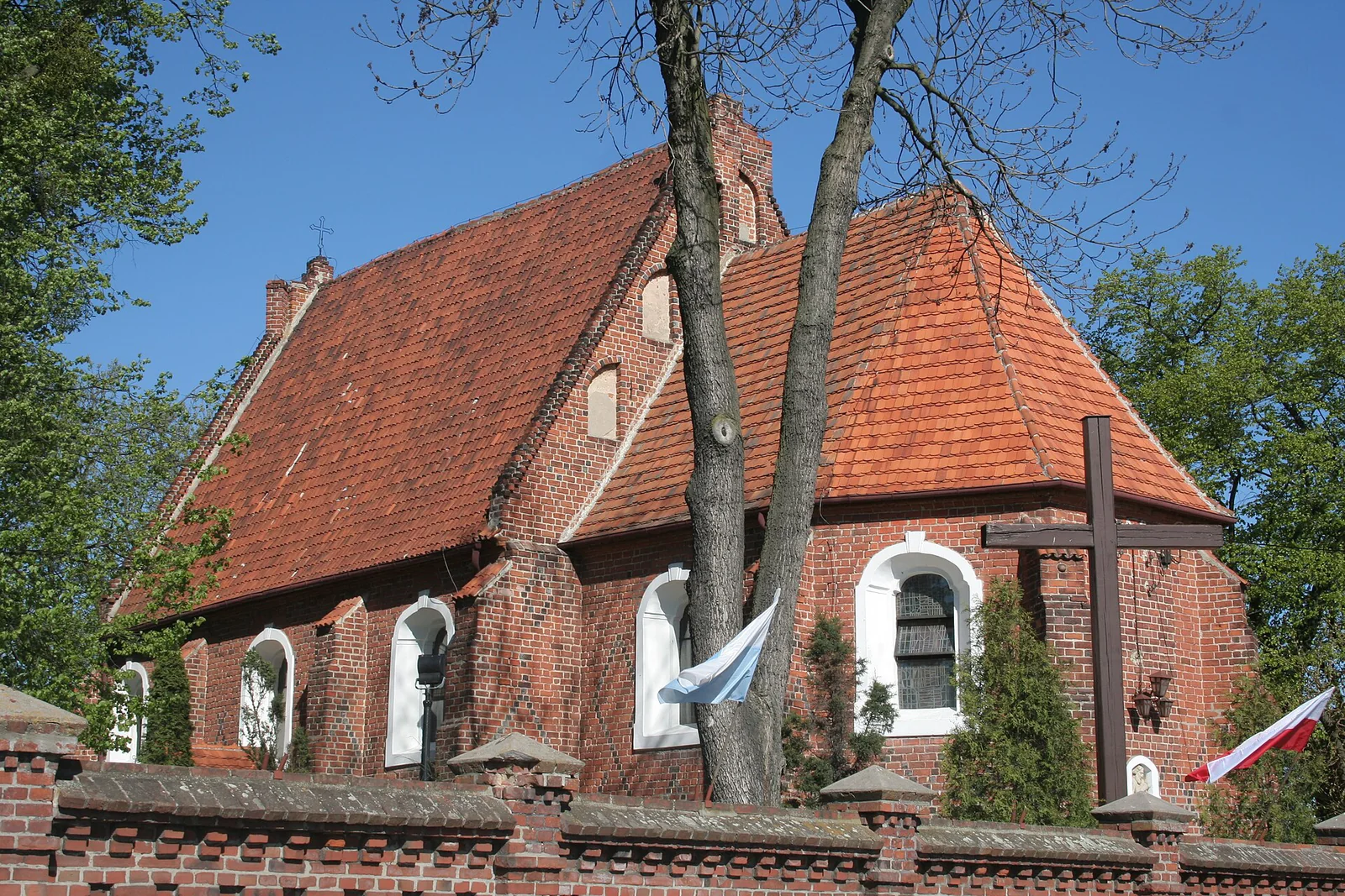 Ceglany kościół świętego Jakuba w Mogilnie z czerwonym dachem, białymi obramieniami okien i drzewami na pierwszym planie