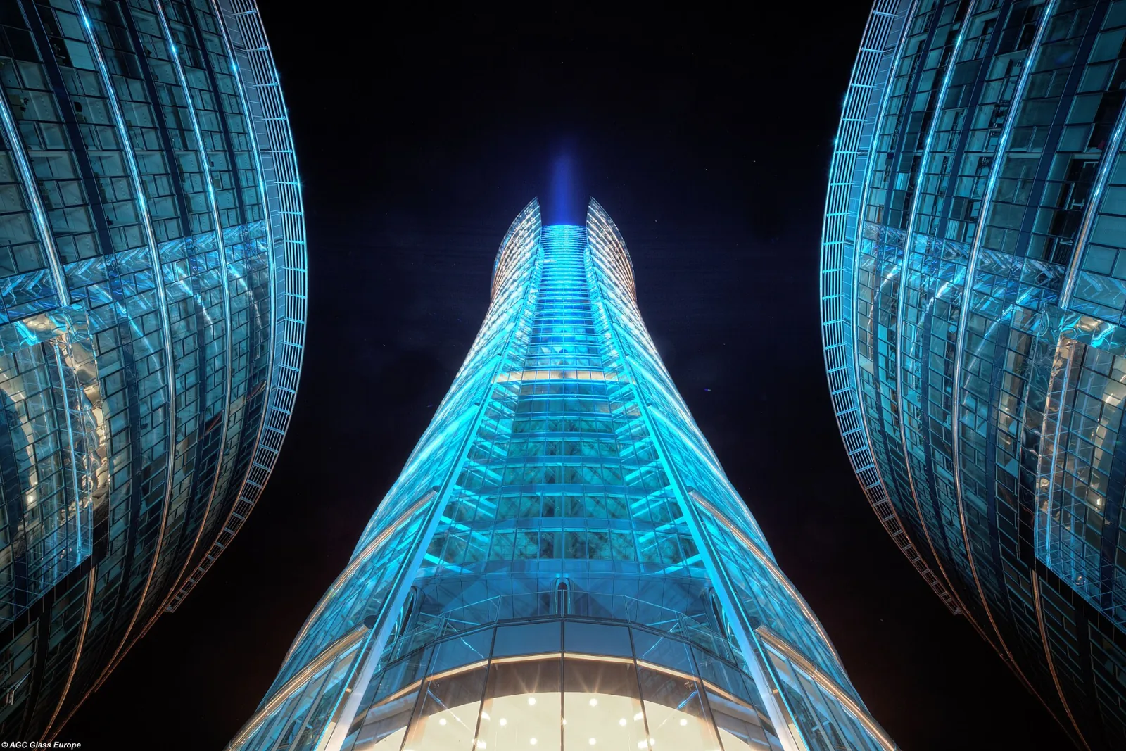 Wieżowiec Warsaw Spire nocą widziany od podstawy z podświetloną na niebiesko szklaną fasadą